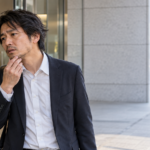 オフィスビルのガラスに映る自分を見ながら、あごの無精ひげや髪の乱れを確かめるスーツ姿の男性