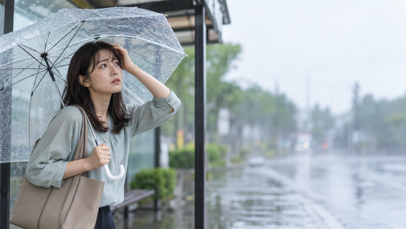 雨のバス停で傘とバッグを持ち、濡れた道路を見ながら立ち止まる女性